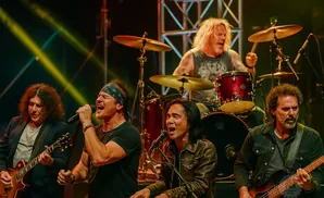 A rock band performs on stage with a guitarist, singer, keyboardist, bassist, and drummer.
