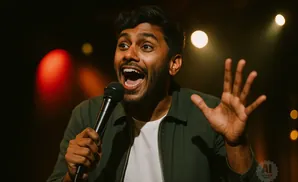 A man holding a microphone on stage, gesturing with his hands and speaking with his mouth open.