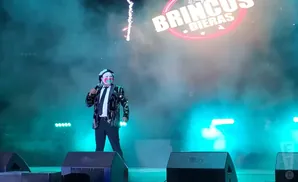 A clown with face paint sings into a microphone on a stage lit with blue and green lights, smoke fills the air.