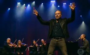 Man with arms raised on stage with an orchestra.