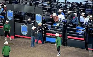 Rodeo clowns and bull riders prepare in a bull riding arena.