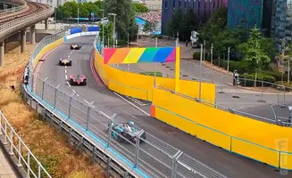 Race cars on a track with yellow barriers and a rainbow banner.