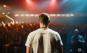 Man on stage facing a crowd, lit by red and blue stage lights.