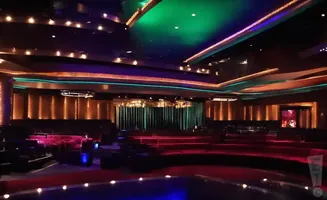 Luxurious theater with red velvet seating, stage with green curtains, and illuminated ceiling.