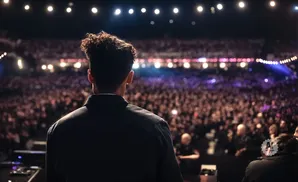 A person stands on stage facing a large crowd at a concert.