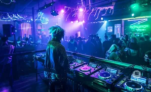 DJ with blue hair playing music at a club with vibrant blue and green lights.