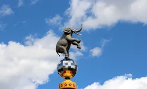 A statue of an elephant balancing on a disco ball against a blue sky with clouds.