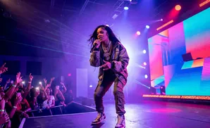 Rapper GloRilla performs on stage, illuminated by purple and green lights, with a cheering crowd in the foreground.