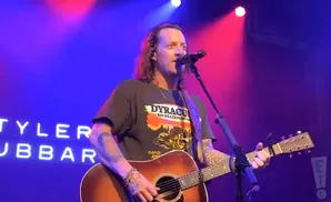 Musician Tyler Hubbard plays guitar and sings on stage with blue and pink stage lighting.