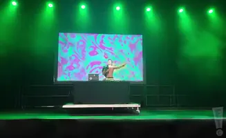 DJ on stage with a colorful background and green spotlights.