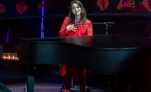 A woman in a red dress sings into a microphone in front of a piano, with a 