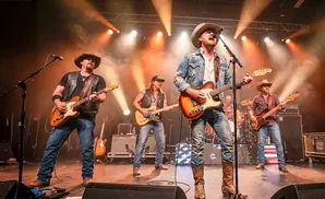 Country band performing on stage, wearing cowboy hats and jeans, playing guitars and bass.