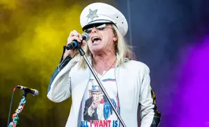A male singer in a white hat and jacket sings into a microphone with a 