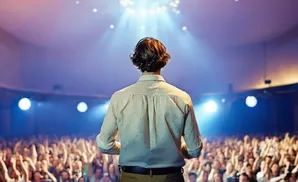 A person on stage with a crowd before them, illuminated by spotlights.