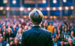 Back view of a person in a suit facing a large, blurred audience.