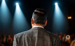 Man in suit facing away from camera, illuminated by stage lights.