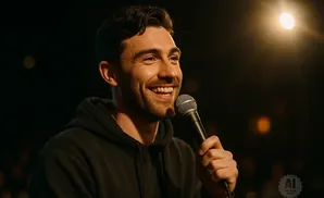 A man in a black hoodie smiles while holding a microphone.