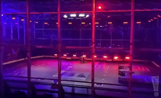 A robot combat arena with purple and red lighting. Two robots are on the arena floor.