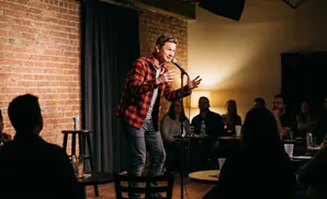 A comedian on stage tells jokes to an audience in a dimly lit club.
