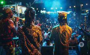 Musicians play brass instruments on stage in front of a crowd at night.