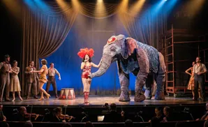 Performers on stage with an elephant and circus tents, an orchestra in the foreground.