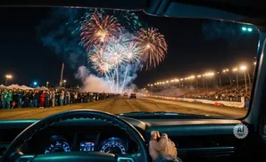 View from inside a car at night, watching fireworks over a drag strip with a crowd watching.