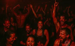 People with red paint on them dance and cheer at a concert.