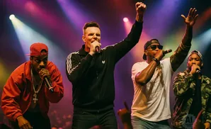 Rappers on stage under purple and yellow lights, holding microphones and gesturing to the crowd.