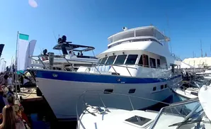 A large white and blue yacht is docked at a sunny outdoor boat show next to other boats and people.