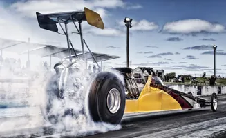 A yellow and red dragster with a large rear wing emits smoke from its tires as it races down a track.