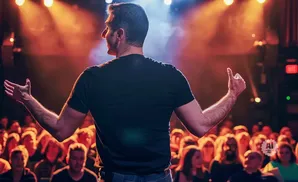 A speaker gestures with his hands to an audience under stage lights.