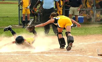 A softball player slides into home plate as the catcher attempts a tag.