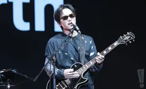 A man in sunglasses sings and plays an electric guitar on stage.