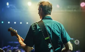 Man playing guitar on stage with bright lights and blurred audience.