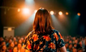 Person in a floral shirt on stage with audience and lights