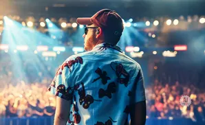 Man in a floral shirt on stage with a crowd and bright lights.