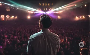 Man on stage facing a cheering crowd under stage lights.