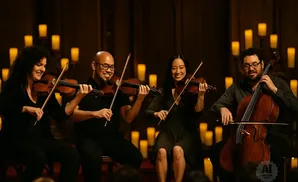 A quartet of musicians playing string instruments in a candlelit room.