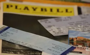A Playbill and tickets on a table, with a postcard of a castle in the background.