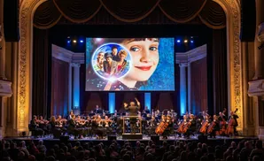 An orchestra performs live to a movie on a large screen in a grand theater.