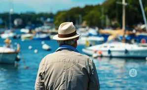 An elderly man in a hat looks out at a harbor filled with boats.