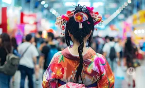 A person in a colorful kimono with elaborate hair ornaments walks through a crowded, blurred indoor market.
