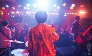 A band performs for a crowd on a dimly lit stage, bathed in red and blue lights.