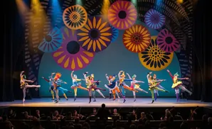 Ballet dancers in colorful costumes perform on stage with a backdrop of large floral patterns.