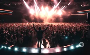 A person on stage raises their arms to a cheering crowd at a concert.