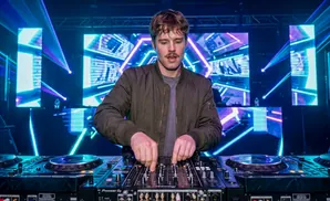 DJ playing music on a mixer with flashing lights and screens in the background.