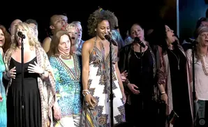A diverse group of singers performing on stage at night.