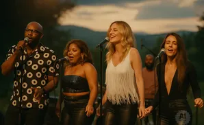 Four singers perform outdoors at dusk with a mountain backdrop.