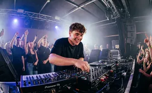 A male singer performs on stage for a crowd, with bright lights and musical equipment.