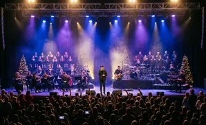 A choir and orchestra perform on stage with Christmas trees and colorful lights.